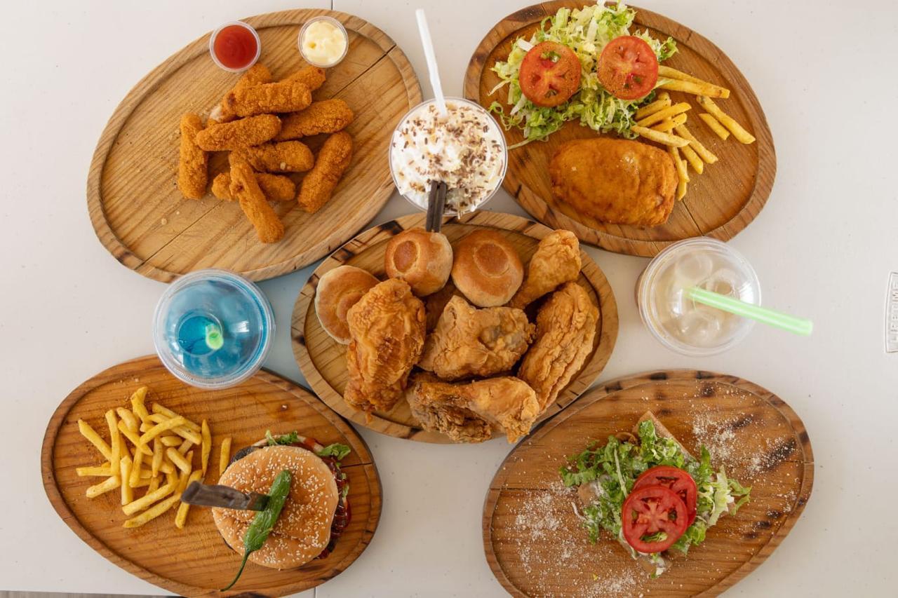 Mesa llena de pollo frito, hamburguesas, snacks y bebidas de Pollón SJR